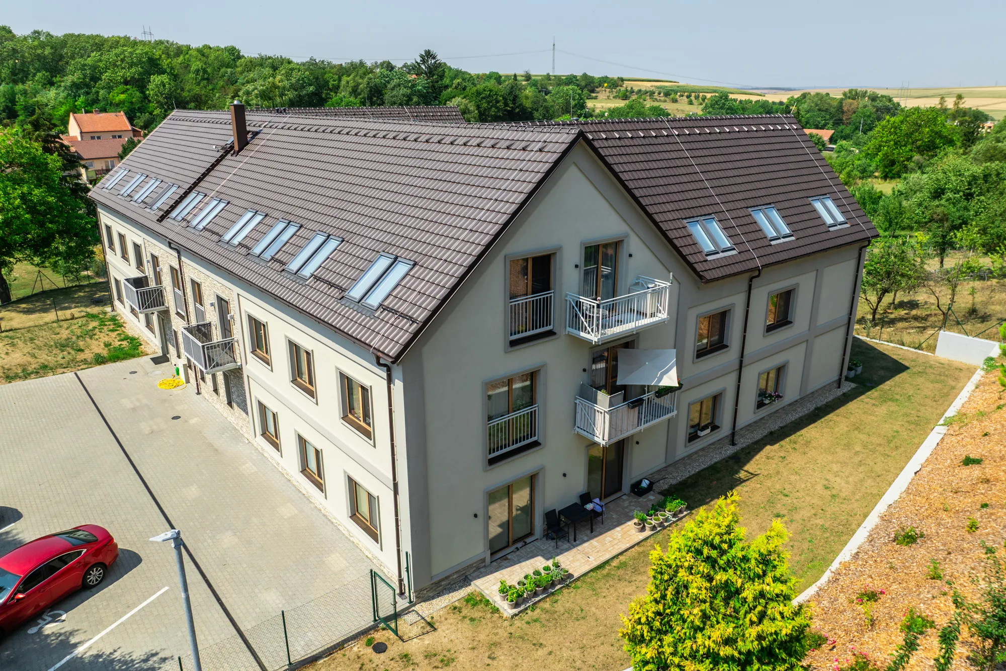 Letecký pohled na bytový dům s parkovištěm a lesem v pozadí